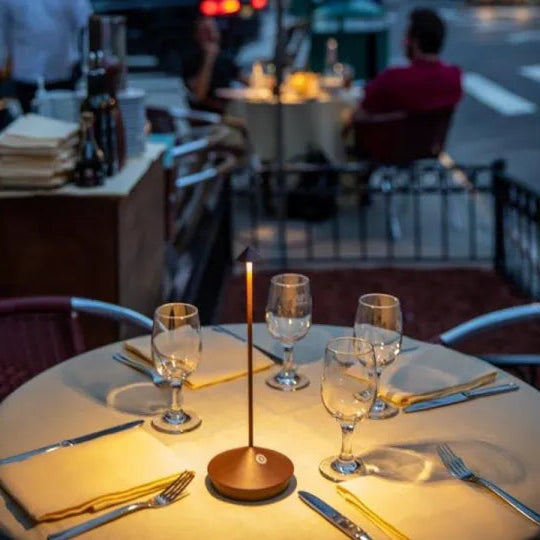Dining table set with glasses, Table lamp, and cutlery in an outdoor restaurant setting.