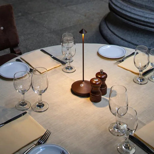 Dining table setup with wine glasses, plates, cutlery, and a small lamp.