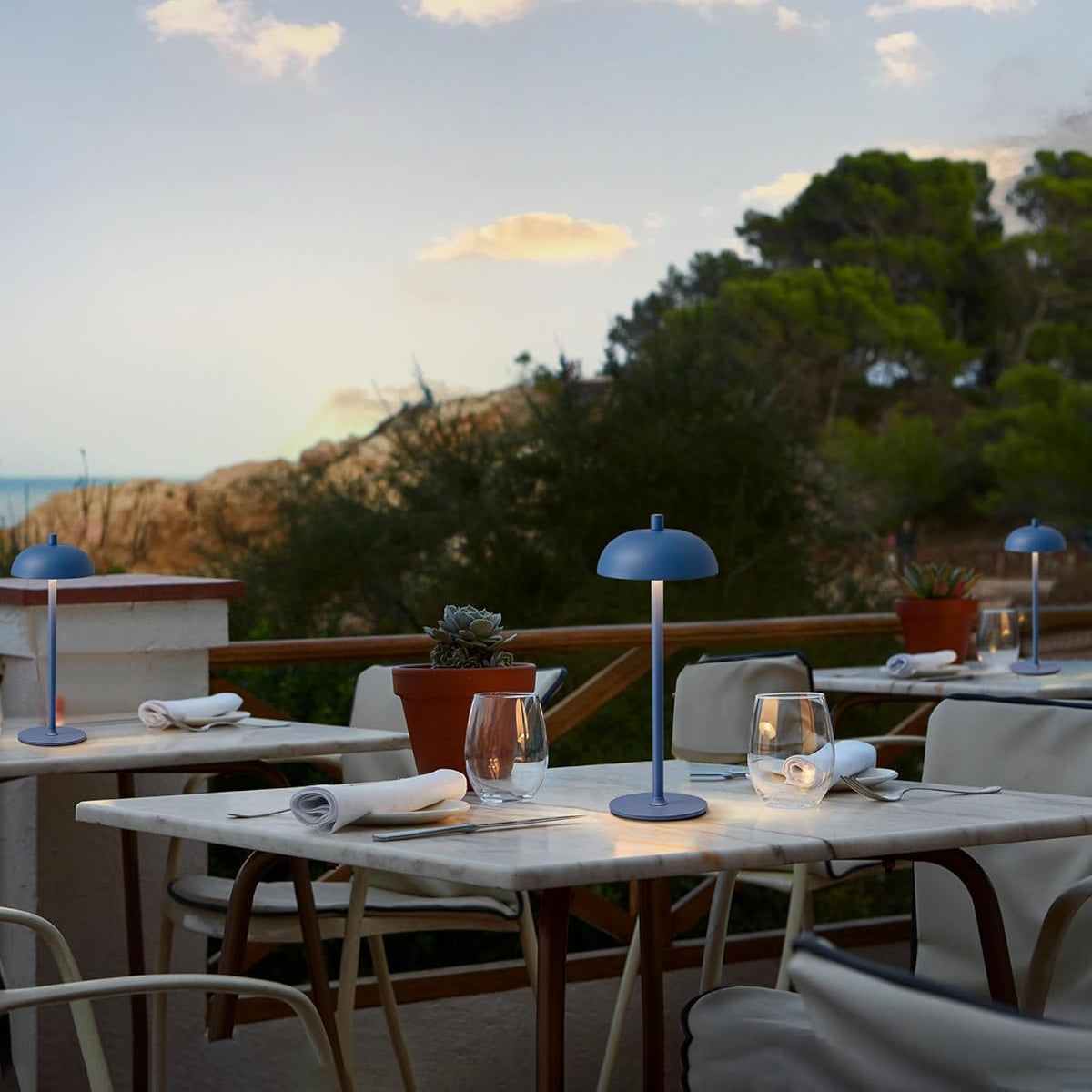 Outdoor dining area with tables, chairs, and blue lamps under a sunset sky.