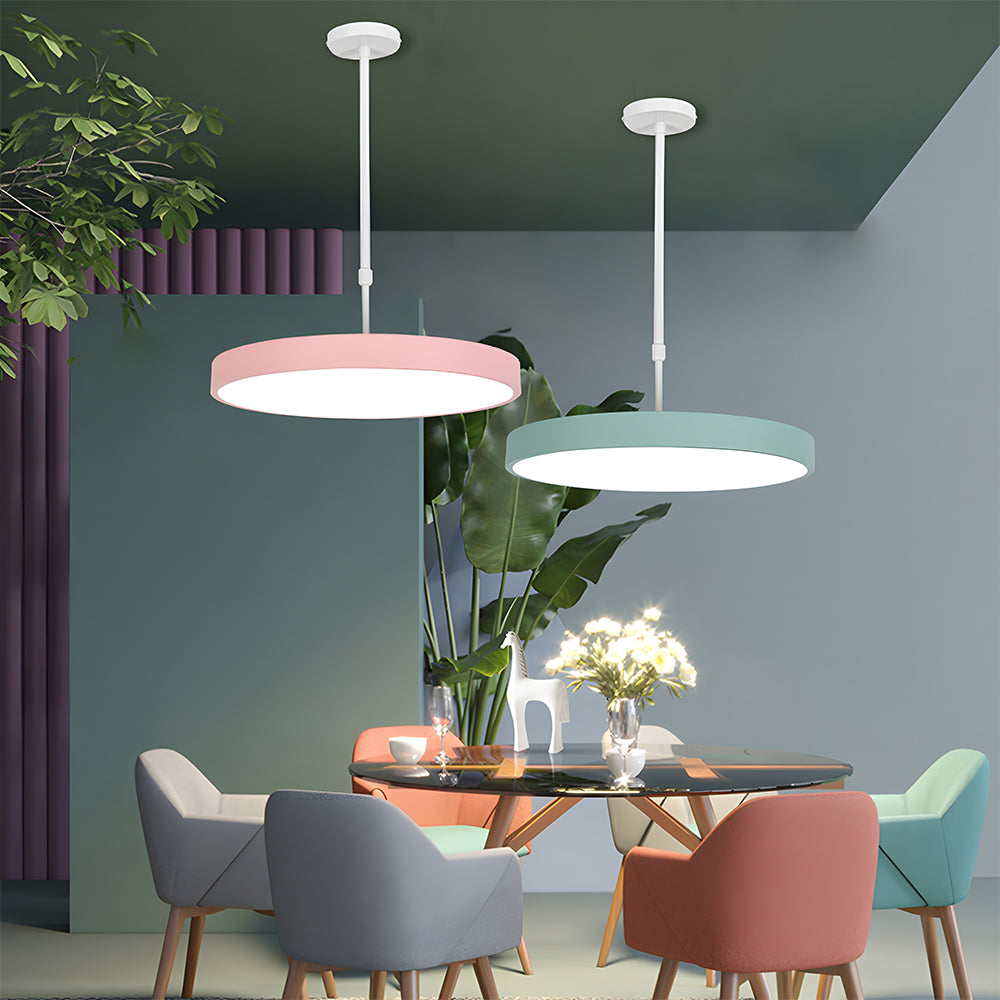 Modern dining room with pink and green pendant lights, colorful chairs, and a glass table.