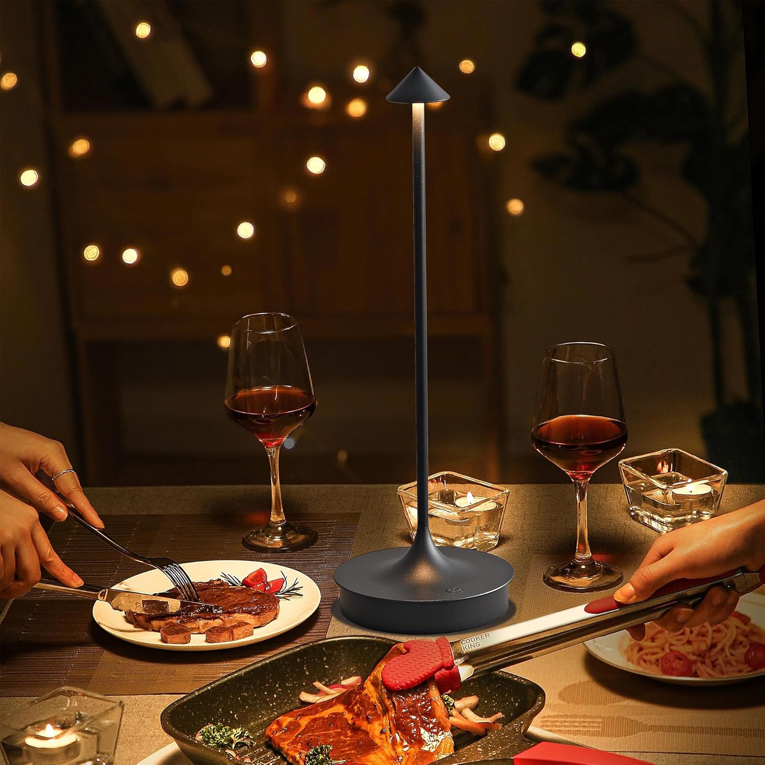 Dinner scene with two glasses of red wine, a plate of food, and a small lamp on a table.