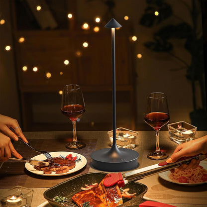 Dinner scene with two glasses of red wine, a plate of food, and a small lamp on a table.