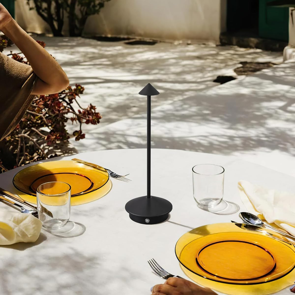 Dining table setting with yellow plates, black stand, and cutlery outdoors.