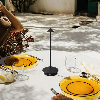 Dining table setting with yellow plates, black stand, and cutlery outdoors.