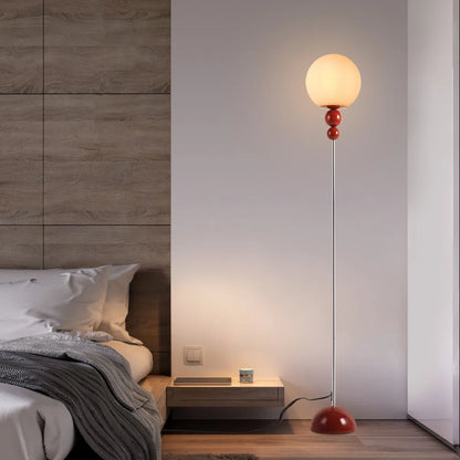 Modern floor lamp with a red base in a bedroom setting.